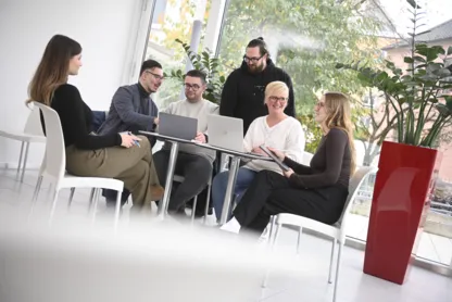 Eine Gruppe Personen sitzen im Kreis um einen Tisch und reden miteinander.