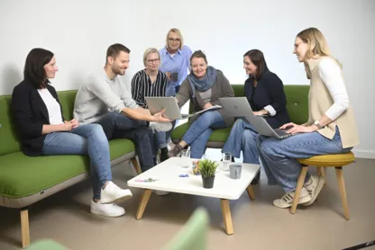 Eine Gruppe Menschen sitzt auf Sofas und schaut sich etwas auf dem Laptop an.